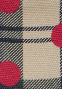 Ύφασμα σε μπεζ και μαύρο καρό με διαγώνιες ρίγες και μεγάλα κόκκινα πουά, που δείχνει υφή υφασμένου υλικού σε κοντινή λήψη.