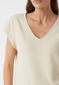 V-hals, kortemouwtop van geribde beige stof met een gestructureerd patroon, met een relaxte pasvorm en zachte val.