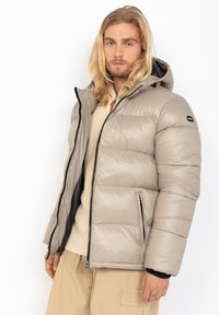 Lichtgrijze pufferjack met capuchon, ritssluiting aan de voorkant, elastische manchetten en zwarte accenten. Ontworpen met een gladde, gequiltte textuur en zijzakken.