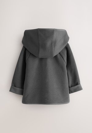 Grå huvtröja i texturerat tyg med huva, utrustad med uppvikta muddkanter och rak fåll. Synliga sömmar och strukturerade designdetaljer.