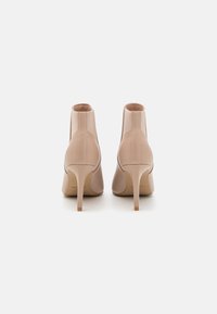 Stivaletti beige con tacchi alti, realizzati in pelle liscia, con punta rotonda e tacco stiletto sottile. Dettagli cuciti e nessun hardware visibile.