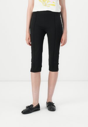 Czarne leggings o długości 3/4 o gładkiej fakturze, z detalami na szwach bocznych i dopasowanym stanem. Zestawione z czarnymi płaskimi butami.