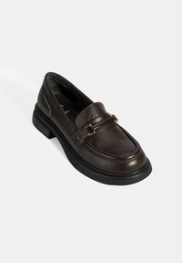 Braune Lederloafer mit abgerundetem Zehenbereich, doppeltem Riemen-Detail, goldfarbenen Hardware-Akzenten und einer stabilen schwarzen Sohle. Glatte Textur.