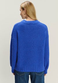 Królestwo niebieski, oversize sweter z miękkiej, strukturalnej dzianiny. Posiada okrągły dekolt i ściągacz na dole. Nosi się go z dżinsami.