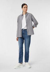 Gestreiftes Hemd in Grau und Weiß, kombiniert mit blauen Jeans und weißen Sneakers. Das Hemd hat lange Ärmel und eine Brusttasche.