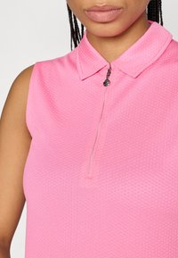 Rožinė atvira be rankovių polo maikutė su tekstūruotu raštu, sulankstytu apykaklės kraštu ir užtrauktuku, kuriame yra apvalus sidabrinis užtrauktuko traukiklis.