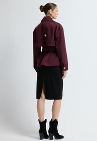 Bordeaux cropped jakke med bælte, over en sort knælængde nederdel med en slids bagpå, parret med sorte ruskinds ankelstøvler.