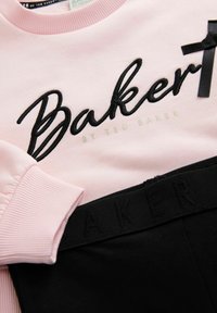 Felpa rosa con logo "Baker" ricamato in nero e dettaglio in raso a fiocco, abbinata a leggings neri con fascia "BAKER" in rilievo.