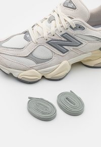 Svijetlosivi i kremasti tenisice napravljene od mrežastog materijala i antilopa, s debljim potplatima i bež naglascima, uz to dolaze i dva para svijetlosivih vezica.