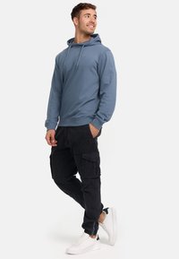 Light blue hoodie with a drawstring, ribbed cuffs, paired with black cargo pants and white sneakers. Simple design without patterns.