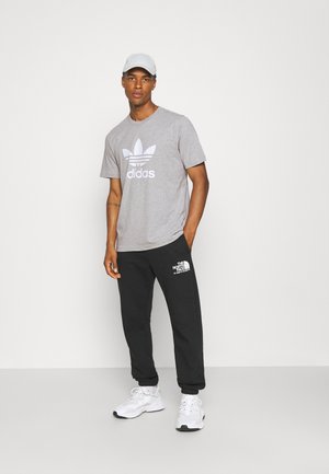 Szara bawełniana koszulka z białym logo Adidas, zestawiona z czarnymi dresami z białym logo North Face, wykończona białymi butami sportowymi.