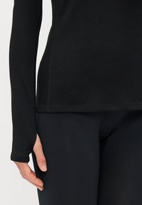 Svart langermet topp med tommelhull, laget av myk, elastisk stoff; kombinert med svarte tettsittende leggings for et strømlinjeformet utseende.