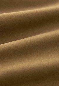 Bruine katoen stof met een gladde textuur, voorzien van subtiele diagonale lijnen en plooien die diepte en beweging creëren.