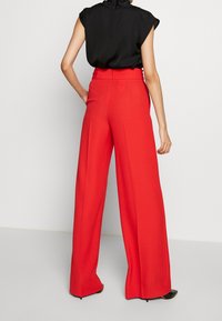 Červené široké kalhoty vyrobené z hladké látky, s vysokým pasem a sklady, v kombinaci s černým bezrukávovým topem.