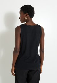 Top negro sin mangas con cuello redondeado, confeccionado en una tela ligera. Presenta un sutil detalle de costura a lo largo del cuello.