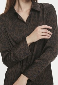 Leopardmönstrad skjorta i brunt och svart, med krage, långa ärmar och knapplockningar vid ärmsluten. Mjuk, slät tygtextur.