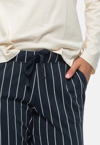 Marinblå randiga byxor i mjukt tyg, med dragsko i midjan, sidofickor och vita vertikala ränder.