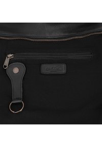 Schwarzer Stoffbeutelabschnitt mit einer horizontalen Reißverschlusstasche, Leder-Schlüsselanhänger mit Metallring und einem geprägten Lederetikett mit dem Schriftzug "Crusell Collection Studio."