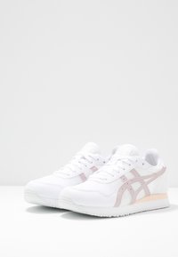 Vita idrottsskor med ovandel i mesh, rosa accenter på sidan och hälen samt en texturerad sula. Har rund tå och snörningsdesign.