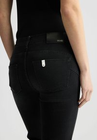 Crne kožne skinny traperice s uskim krojem i suptilnim šavovima. Karakteristike uključuju stražnje džepove i oznaku s logotipom na pojasu.