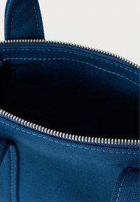 Τσάντα από ύφασμα ναυτικού μπλε με φερμουάρ, με λευκή ραφή και ανάγλυφη επιφάνεια. Το εσωτερικό έχει σκοτεινή επένδυση.