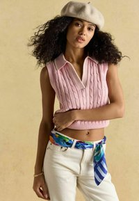 Rózsaszín, kötött, ujjatlan felső fehér gallérral, fehér farmerral és a deréknál megkötött, több színű mintás sállal párosítva.