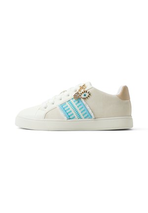 Weißer Sneaker mit blau gemustertem Streifen, Schnürdesign, beigefarbenem Fersenpatch und goldfarbenem Ösen- und Handanhänger nahe den Schnürsenkeln.