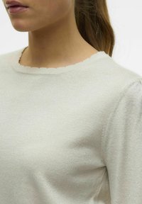 Pull en maille gris clair avec une finition texturée, doté d'un col festonné et de manches légèrement bouffantes, fabriqué en tissu doux.