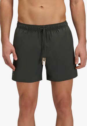 Homme portant un short de bain vert foncé uni avec une taille élastique et un cordon noué, debout, les bras détendus le long du corps.