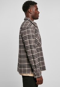 Grijs en zwart geruit flanellen shirt met een knopsluiting aan de voorkant, lange mouwen en een enkele borstzak. Geverfd stof met een comfortabele pasvorm.