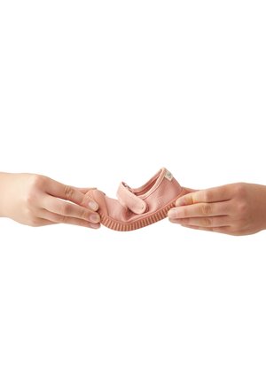 Pink children's shoe with a soft fabric design, Velcro strap, and textured rubber sole, held between two hands against a white background.