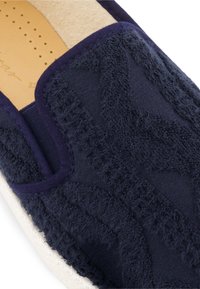Marine slip-on schoen van textiel, met een zachte oppervlakte en een beige voering. Rubberen zool met beige rand en decoratieve stiksels.