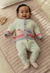 Šviesiai žalias megztas kardiganas su žaisminga siuvinėjimu, rožinėmis detalėmis ir mediniais mygtukais. Derančios tekstūruotos kelnės šviesiai žalia spalva. Minkšta, jauki medžiaga.