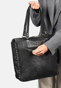 Zwarte leren tote bag met studs, twee stevige handvatten en een voorzak met rits. Zacht, gestructureerd oppervlak met een strakke vorm.