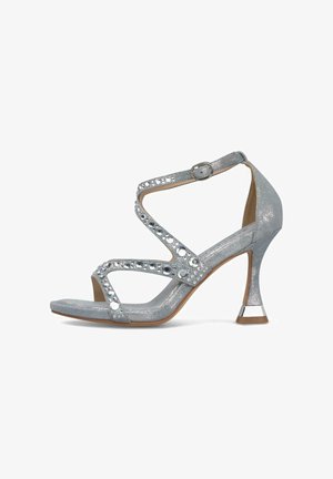 Sandale argentée à talon haut avec des brides croisées ornées de strass, une boucle à la cheville et un talon fin à la forme unique.