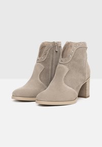Beige Knöchelstiefel aus Wildleder mit Netzseiten, Reißverschluss, dekorativen Nieten und einem gestapelten Absatz. Glatte Textur mit detailliertem Design.