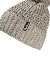Beanie beige lavorato a maglia con motivo a costine e un pom-pom sulla parte superiore. Presenta un'etichetta nera con testo bianco sul lato.