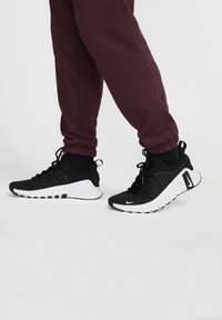 Svarta sportskor med vita sulor, textilmaterial och kontrasterande Nike-logga. Kombinerade med bordeauxfärgade joggers, elastiska manschetter synliga.