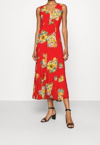 Röd ärmlös klänning med V-ringning, med ett blommönster i gult och grönt. Utsvängd fåll, lätt tyg, i kombination med svarta blockklack-sandaler.