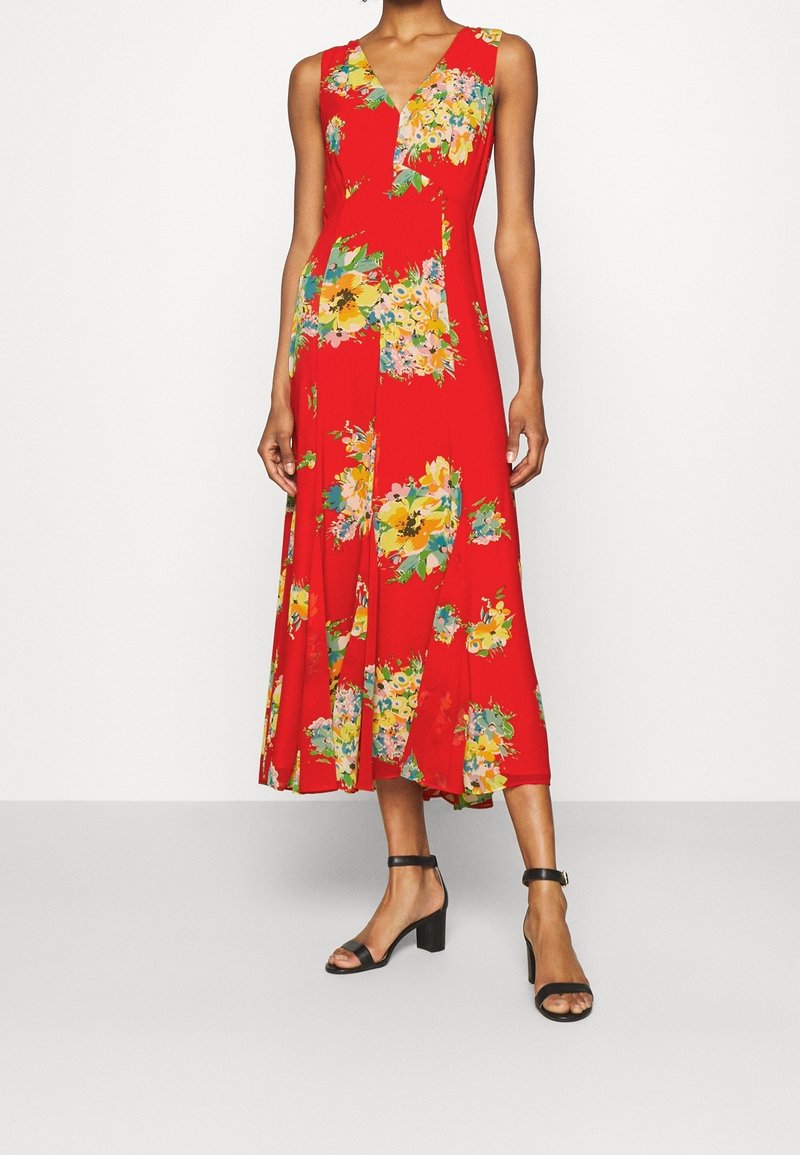 Röd ärmlös klänning med V-ringning, med ett blommönster i gult och grönt. Utsvängd fåll, lätt tyg, i kombination med svarta blockklack-sandaler.