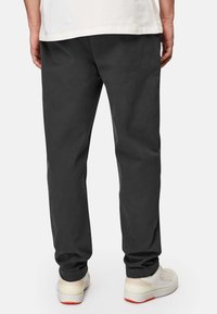 Black, straight-leg pants with a smooth texture, cotton material, and simple design. Paired with cream sneakers featuring orange soles.