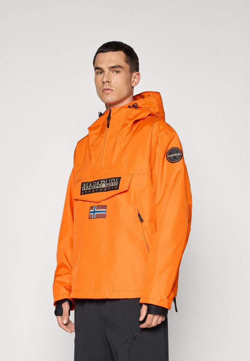 Giacca impermeabile arancione con tasca frontale, cappuccio regolabile e logo ricamato. Presenta una patch a forma di bandiera e accenti neri a contrasto.