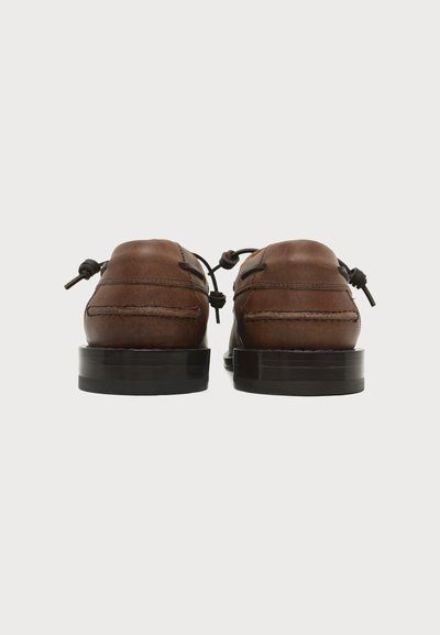 Paire de mocassins en cuir marron avec semelles noires vue de dos, montrant des lacets en cuir noués et des détails cousus.