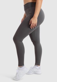 Hoch taillierte graue Leggings aus dehnbarem Stoff, mit einer glatten Textur und einer figurbetonten Silhouette. Getragen mit weißen Sportschuhen.