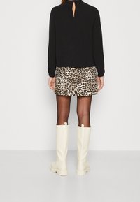 Zwarte blouse met lange mouwen en sleufdetail bij de hals, gecombineerd met een mini-jurk in luipaardprint en witte kniehoge laarzen.