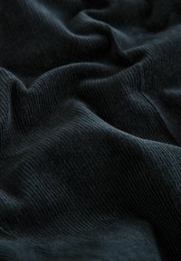 Černá texturovaná látka s žebrovanými vzory, která má měkké, vlnité záhyby vytvářející dojem hloubky a pohybu.