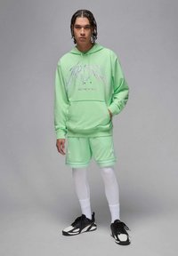 Felpa verde chiaro con stampa grafica, abbinata a pantaloni corti in rete dello stesso colore. Collant bianchi e scarpe da ginnastica nere completano l'outfit.