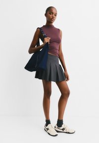 Donkerdenim schoudertas, aansluitend bordeauxkleurig mouwloos topje, geplooide grijze rok en crèmekleurige sneakers met zwarte accenten. Gladde texturen en casual ontwerp.