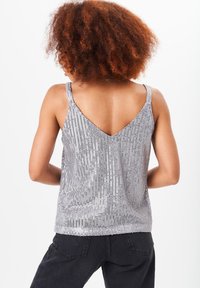 Silver sequined tank top with a V-shaped back, featuring vertical stripes and thin shoulder straps, paired with dark pants.