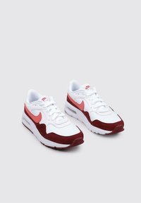 Weiße Sneaker mit roten Wildlederakzenten, pinkem Logo und Schnürdesign. Verfügt über eine sichtbare Luftdämpfungseinheit in der Sohle.